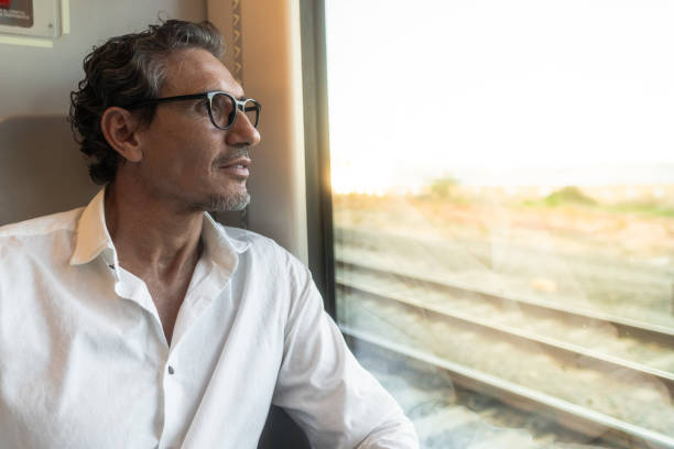 Mature businessman sitting on a train looking out the window while sun shines