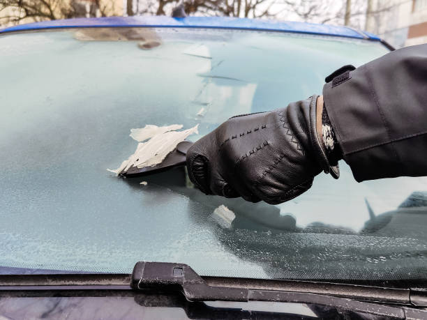 istock Cleaning car windows in winter. Man scrapes hoarfrost with a plastic scraper from the windshield of a blue car. Hand in a black leather glove in the cold. Close-up. Selective focus. 2167481227