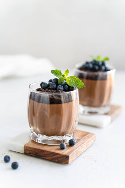 istock Delicious chocolate mousse or pudding with chocolate cookie crumbs, fresh blueberry and mint in glasses on a light concrete background. Confectionery menu, glass dessert recipe. Vertical 2167485270