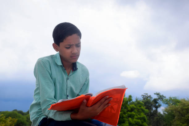 istock a cute boy reading book outdoor with sky background 2167494934
