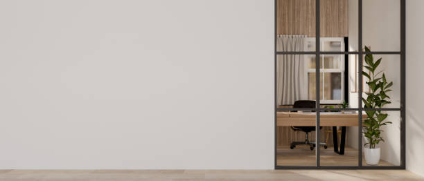 A modern hallway features an empty white wall and a glass partition that looks into a private office