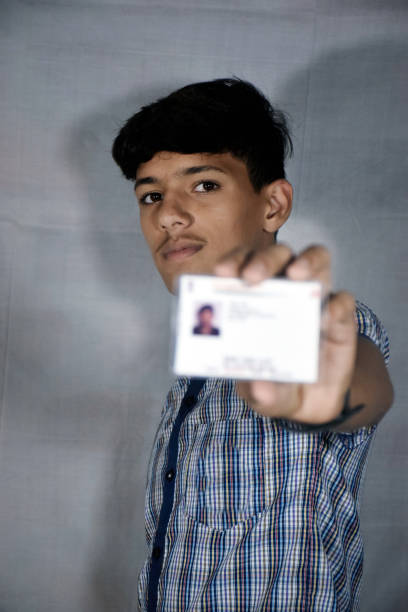 istock Indian school boy wearing dark blue school uniform, with smiling face shows his blurred aadhar card in his hand. 2167495685