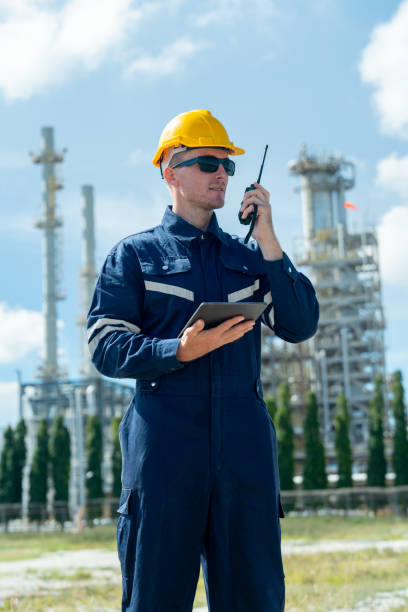 istock Vertical image of factory engineer or technician worker man hold walkie-talkie also hold tablet in other hand and stand in front of refining and petrochemical factory with day light. 2167502316