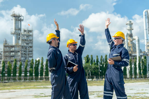 istock Three factory engineer or technician workers raise hands up to express happiness and stand in front of refining petrochemical factory and tank with day light. 2167502321