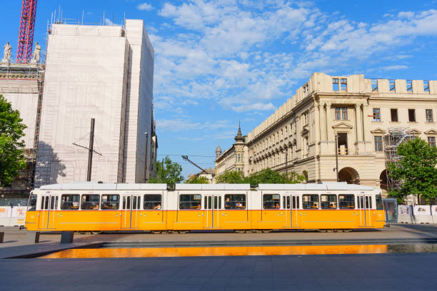 Budapest, Hungary - July 7, 2024: Yellow tram traveling past a historic building under renovation in Budapest.