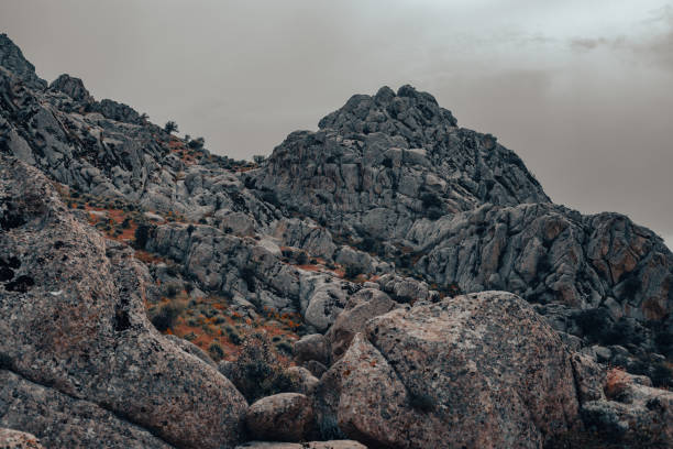 A rocky mountain range with a cloudy sky in the background. The rocks are large and jagged, giving the scene a rugged and wild appearance. The clouds in the sky add a sense of depth