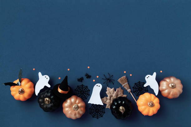 Halloween party decorations from pumpkins, bats, spider web, ghosts on dark blue background top view. Happy halloween holiday greeting card.