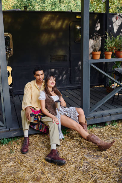 A young couple relaxes by their camping van, savoring the tranquility of the surrounding forest.