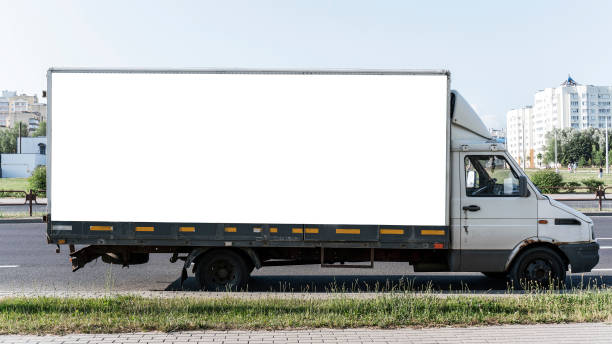 istock Side view of delivery truck with large blank white panel on its cargo area parked on side of road. Truck is slightly worn and urban background includes greenery and residential buildings 2167524829