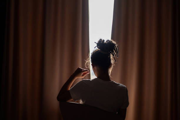 Person silhouetted sitting against light while peering through curtains.