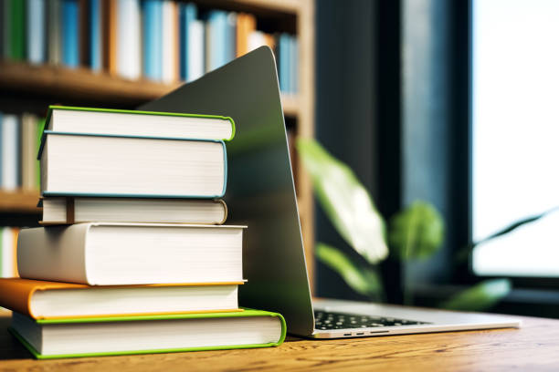 Stack of books next to an open laptop on a wooden desk in a library. Blurred bookshelf background. Concept of education and online study. 3D Rendering