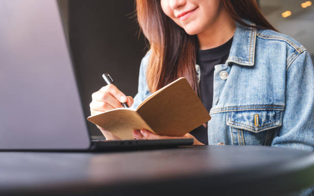istock Closeup image of a young woman writing on a notebook while working on laptop computer 2167530384
