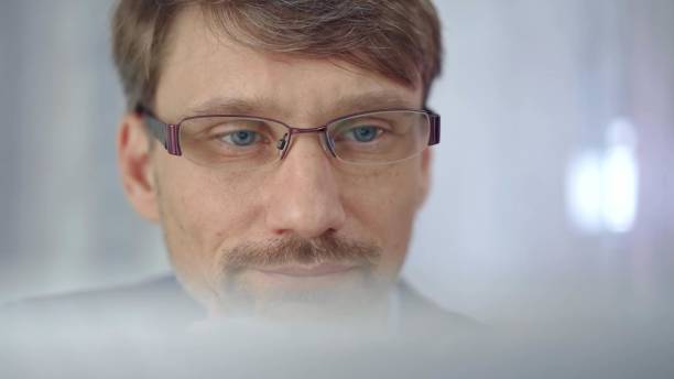 Businessman with glasses looking intently obscured partially by a translucent surface of laptop. Business people concept.
