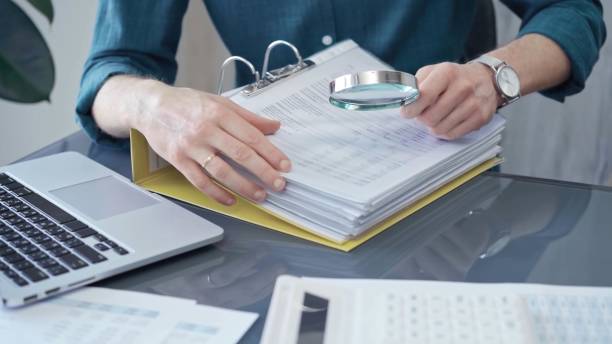 istock Businessman or professional auditor is analyzing data sheets. Close-up of an bookkeeper's hand with magnifying glass inspecting financial reports. Business audit and taxes 2167537434