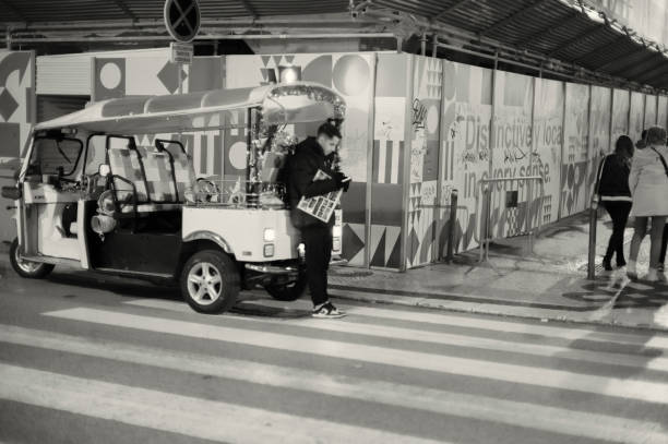 Lisbon, Portugal - December 23, 2023: A tuk-tuk driver checks his cell phone while waiting for clients at a corner in Lisbon downtown.