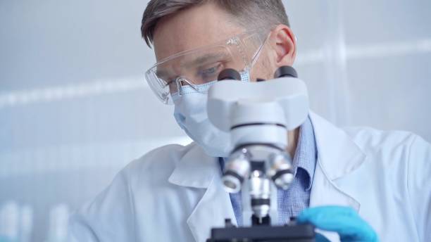 istock Man scientist with protective glasses, mask and gloves is using microscope in laboratory, portrait of researcher. Microbiology science concept 2167543430