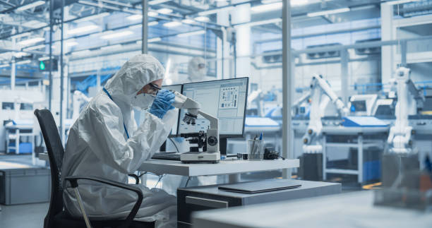 istock Modern Factory: Industrial Engineer Working on Desktop Computer in Clean Sterile Coveralls. Scientist Using a Microscope, Developing Advanced Solutions for High-Tech Medical Vaccine and Gene Research 2167547022