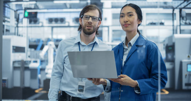 istock Industrial Engineers Working at a Technology Factory. Caucasian Man and Asian Female Using Laptop Computer and Having a Conversation. Footage with a Portrait of a Couple of Employees at a Plant 2167547061