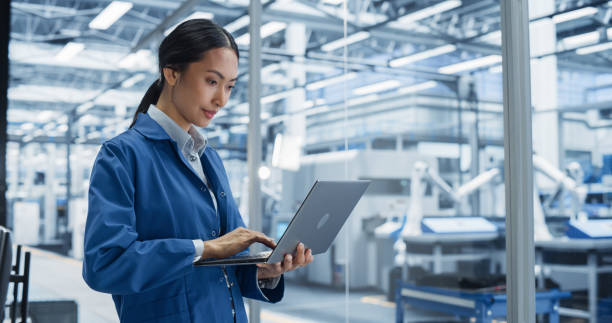 istock Portrait of Beautiful Electronics Manufacturing Technician Working on a Laptop Computer at a Factory. Asian Female Specialist Developing, Maintaining, Setting Up Programs for Machine Production 2167547480