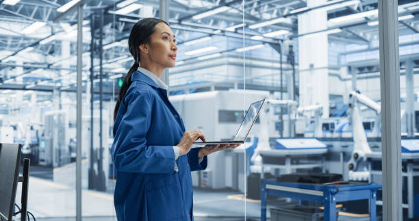istock Southeast Asian Engineer Using Laptop Computer and Looking Around a Factory Facility with Equipment Producing Modern Electronic Components for Advanced Industrial Productions 2167548039