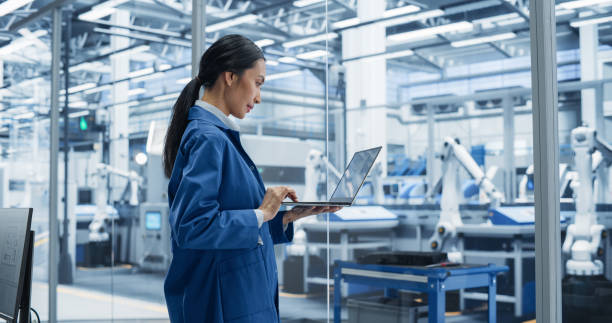 istock Southeast Asian Engineer Using Laptop Computer and Looking Around a Factory Facility with Equipment Producing Modern Electronic Components for Advanced Industrial Needs 2167548061