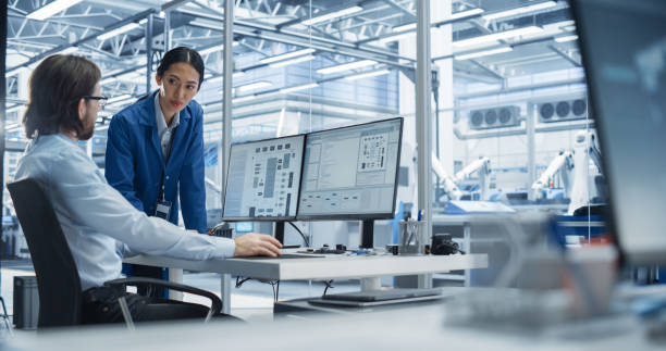 istock Portrait of a Young Male Engineer and a Asian Team Leader Collaborating on a Project, Using Computer and Talking in a Factory with Equipment Producing Modern Technical Devices for Tech Industries 2167548217