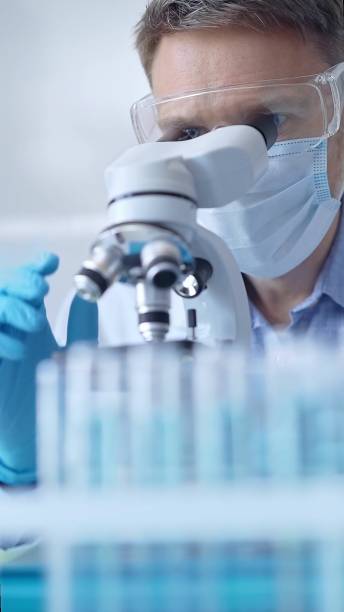 istock Man scientist with protective glasses, mask and gloves is using microscope in laboratory, vertical portrait of researcher. Microbiology and science 2167548489