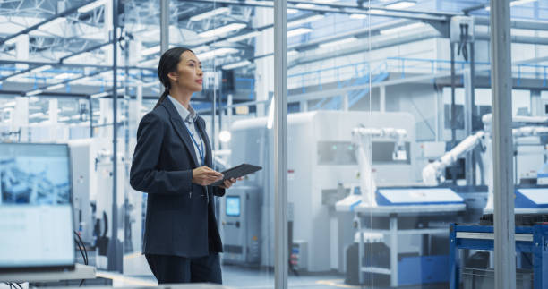 istock Thoughtful Asian Engineer Walking with a Tablet Computer, Monitoring Conditions at an Automated Electronics Assembly Line with Robot Hands Working with the Help of Artificial Intelligence Software 2167548739