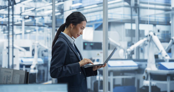 istock Production Line Technician Working on a Laptop Computer at a Factory Office. Asian Female Software Specialist Updating Code for Machine Production and Assembly with Automated Robotic Arms 2167548801