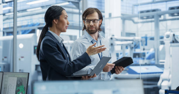 istock Industrial Engineers Working at a Technology Factory. Caucasian Man and Asian Female Using Laptop and Tablet Computers and Having a Conversation. Footage with a Portrait of a Couple of Employees 2167548891