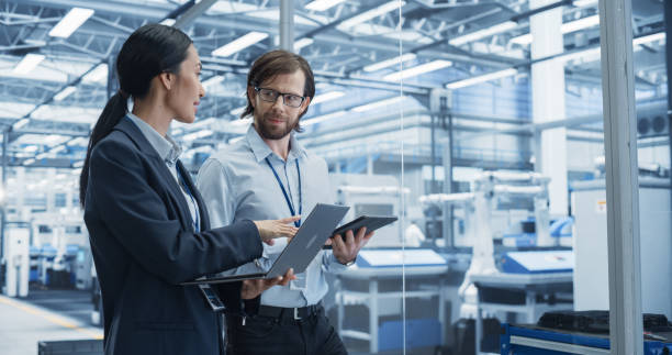 istock Portrait of a Cheerful Engineer and Happy Asian Scientist Using Laptop and Tablet Computers, Talking in a Factory Facility with Robots Producing Modern Electronic Components for Different Industries 2167548971