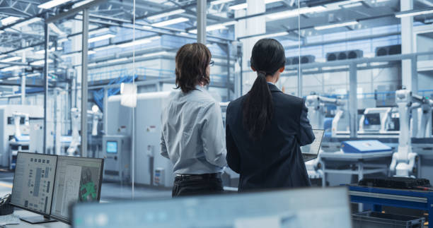 istock Young Caucasian Engineer and Asian Technician Having a Conversation and Using a Laptop Computer. Specialists Monitoring, Analyzing Conditions at a Modern Electronics Factory with Automated Conveyor 2167549046