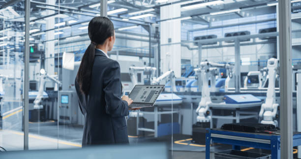 istock Electronics Manufacturing Technician Working on a Laptop Computer at a Factory Space. Asian Female Specialist Developing, Maintaining, Fine-Tuning Programs for Machine Production and Assembly 2167549054