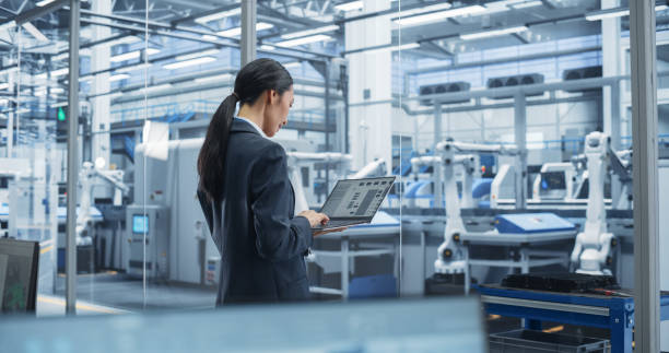 istock Southeast Asian Engineer Using Laptop Computer and Looking Around a Factory Facility with Equipment Producing Modern Electronic Components for Different Industries. Footage From the Back 2167549061
