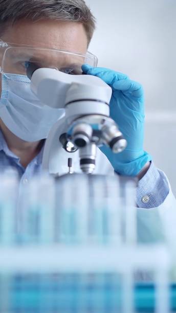 istock Man scientist with protective glasses, mask and gloves is using microscope in laboratory, vertical portrait of researcher. Microbiology and science 2167551487