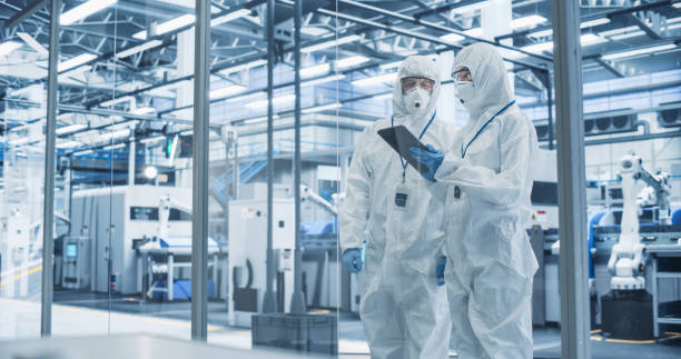 istock Development Factory Cleanroom: Engineers Wearing Coveralls and Goggles while Talking and Using Tablet. Scientists Working in Advanced Electronics Manufacture with Precision Machinery 2167551901