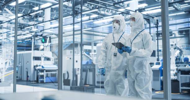 istock Development Factory Cleanroom: Engineers Wearing Coveralls and Goggles while Talking and Using a Tablet Computer. Scientists Working in Advanced Electronics Manufacture with Precision Machinery 2167551926