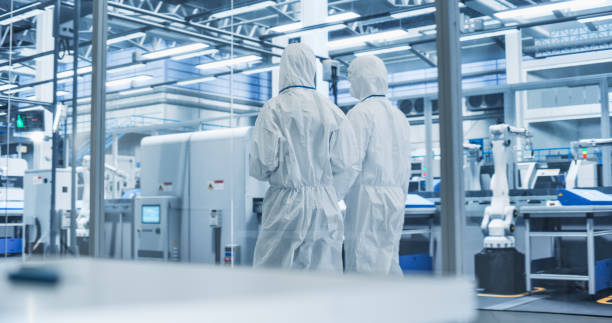 istock Sterile Modern Factory: Professionals in Coveralls Having a Conversation while Walking Through a Plant. Medical Electronics Manufacturing Laboratory with CNC Machinery and Automated Robotic Arms 2167551952
