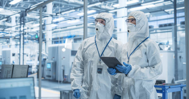 istock Industrial Scientists Wearing Disposable Protective Suits, Masks and Goggles at Production Plant. Specialist Using Tablet Computer, Analyzing Potential Work Hazards and Contamination at a Workplace 2167551994