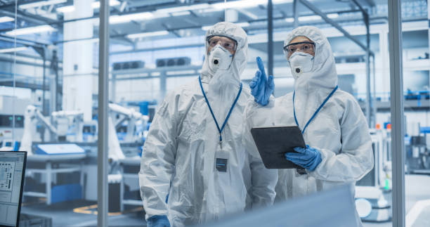 istock Industrial Scientists Wearing Disposable Protective Suits, Masks and Goggles at a Production Plant. Specialist Using Tablet Computer, Analyzing Potential Work Hazards and Contamination at a Workplace 2167552021