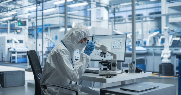 istock Research Factory Cleanroom: Engineer Wearing Coveralls, Gloves, and Goggles while Using Microscope to Inspect a Microchip. Scientist Developing an Advanced Electronics Component for Precision Industry 2167552081