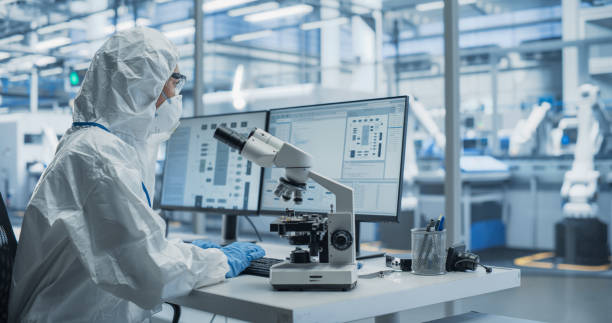 istock Research Factory Cleanroom: Engineer Wearing Coveralls, Gloves and Goggles while Using Microscope to Inspect a Microchip. Scientist Developing Advanced Electronics Component for the Precision Industry 2167552097