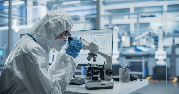 istock Research Factory Cleanroom: Engineer Wearing Coveralls, Gloves and Goggles while Using Microscope to Inspect a Microchip. Scientist Developing an Advanced Electronics Component for Precision Industry 2167552113