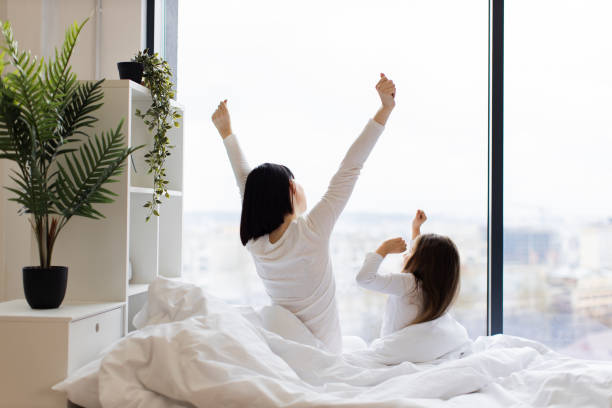 istock Mother and daughter stretching in bed by large window 2167552204