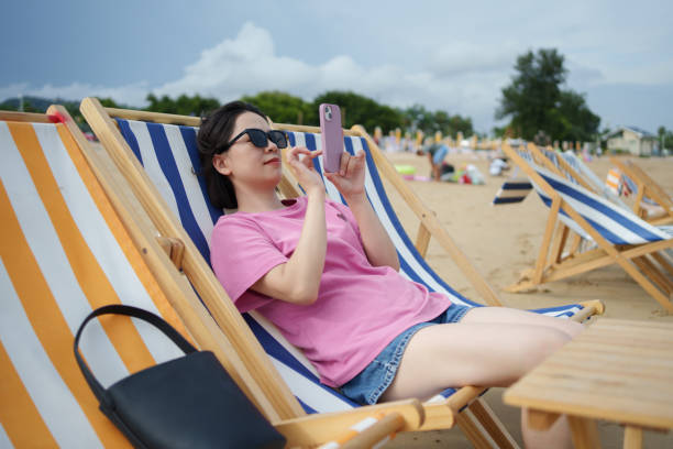 istock Woman sitting on beach chair using smartphone 2167552304