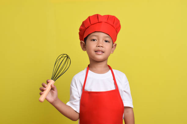 istock Cute little chef holding kitchen whisk. Asian boy wearing red apron 2167555622