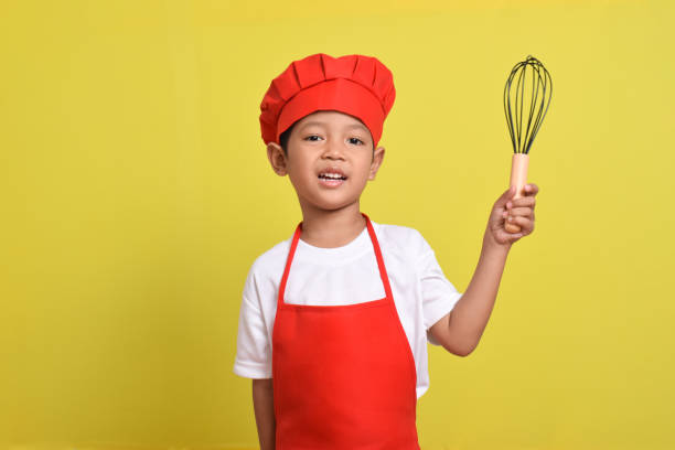 istock Cute little chef holding kitchen whisk. Asian boy wearing red apron 2167555896
