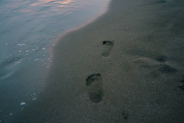 Men legs leaving footprints on the sandy beach.