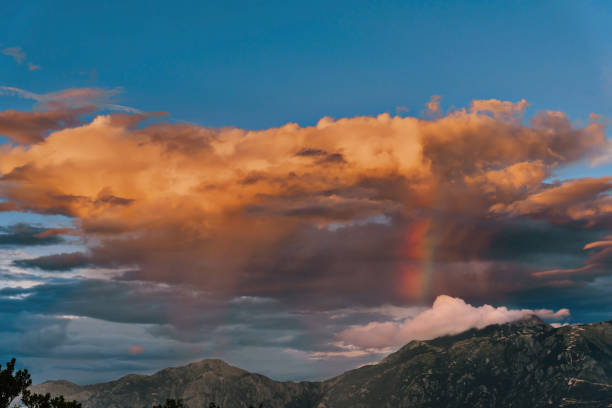 Mountain landscape with a rainbow in front of the Aineck mountain on the border of Salzberg and Carinthia in the Central Eastern Alps during an overcast springtime day in Austria.
