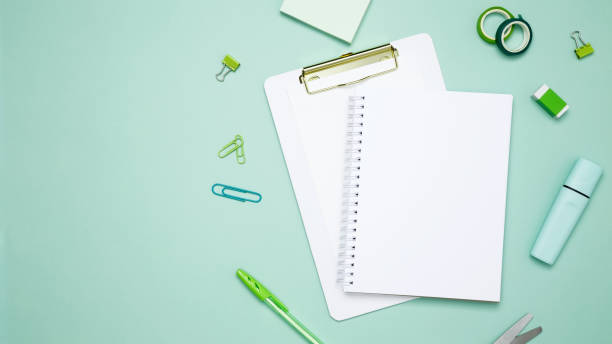 istock Creative flat lay mockup design of workspace. Top view composition with white notebook, to do list and stationery on green background 2167574223